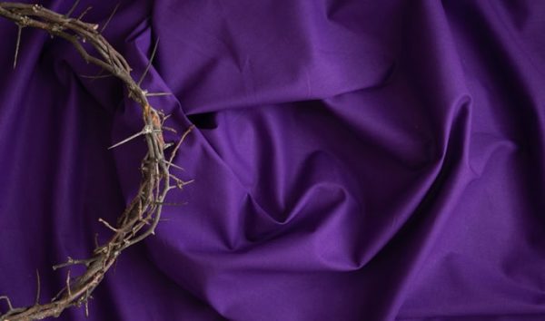 Partial crown of thorns border on a dark purple fabric background with copy space, shot from above